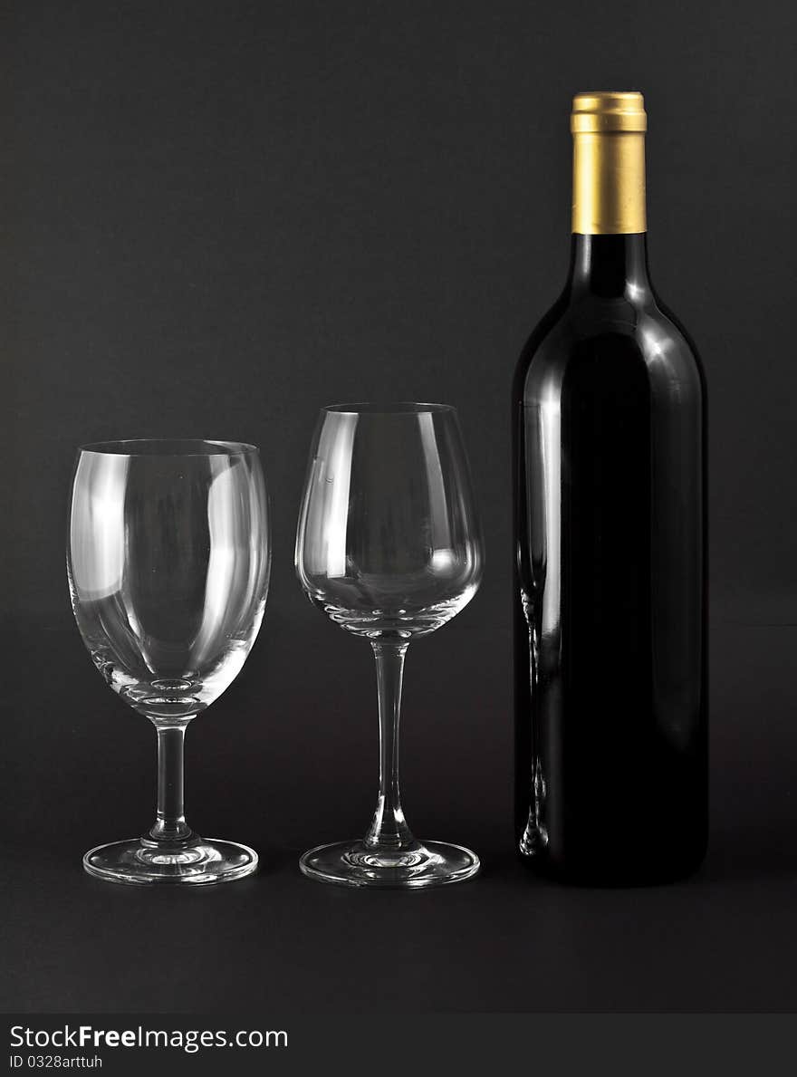 A bottle of red wine and two elegant glasses on black background