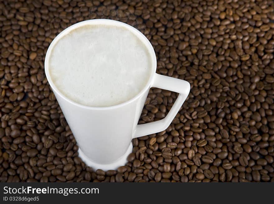 Coffee time - mug filled with hot coffe with cream on brown beans background. Coffee time - mug filled with hot coffe with cream on brown beans background