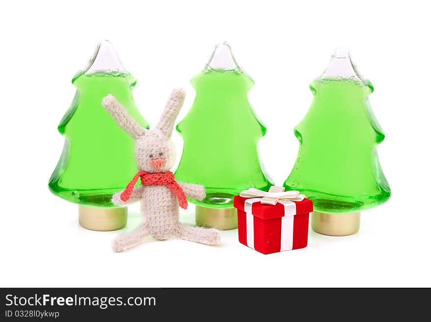 Knitted rabbit and a red box gifts to the background of three green bottles in the shape of a Christmas tree