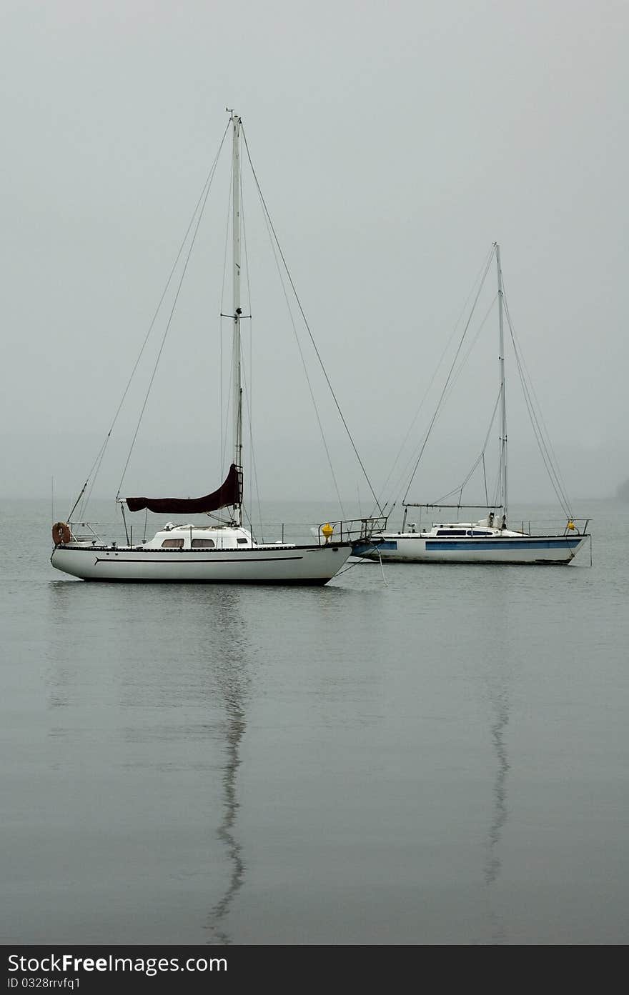 Two boats sit on a lake surrounded by mist and the reflections of their masts on the water. Two boats sit on a lake surrounded by mist and the reflections of their masts on the water