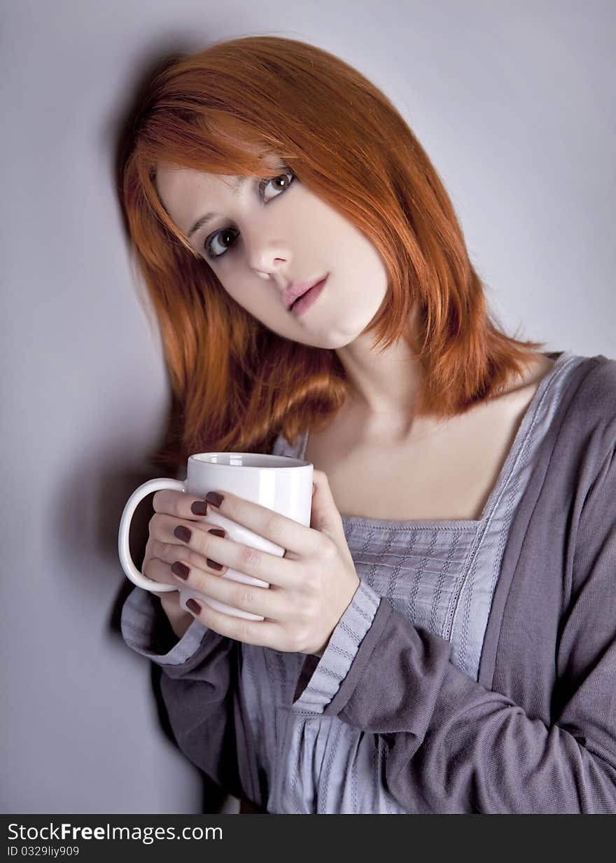 Portrait of red-haired girl with cup. Studio shot.