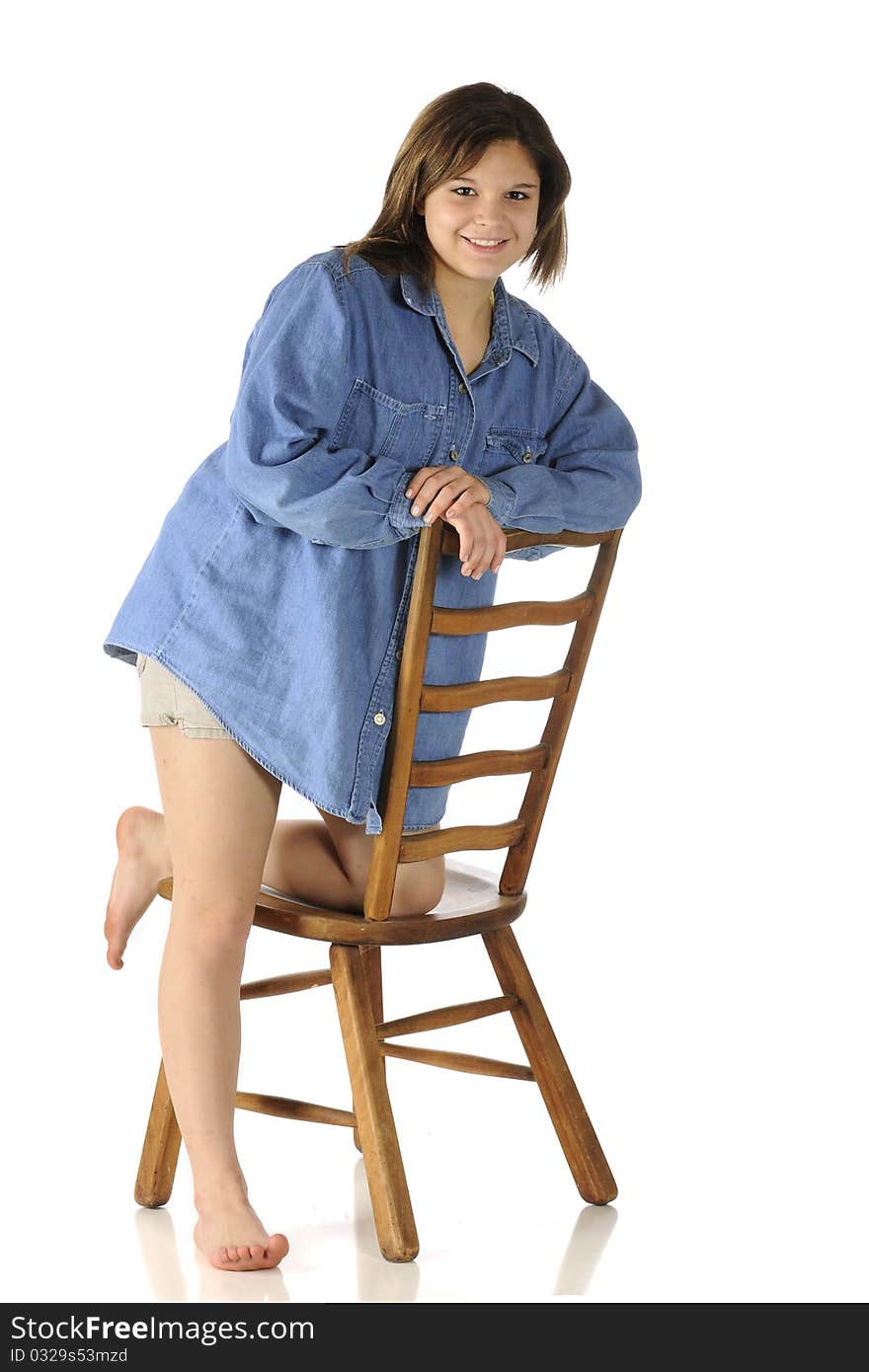 A beautiful barefoot teen in shorts and an over-sized denim shirt leaning on a ladder-back chair. A beautiful barefoot teen in shorts and an over-sized denim shirt leaning on a ladder-back chair.