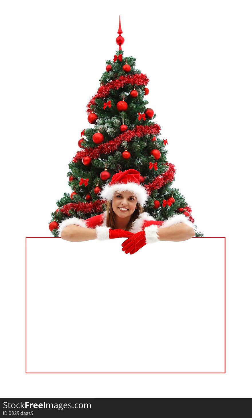 Female Santa with red hat and gloves, smiling over a white billboard near the Christmas tree. Female Santa with red hat and gloves, smiling over a white billboard near the Christmas tree