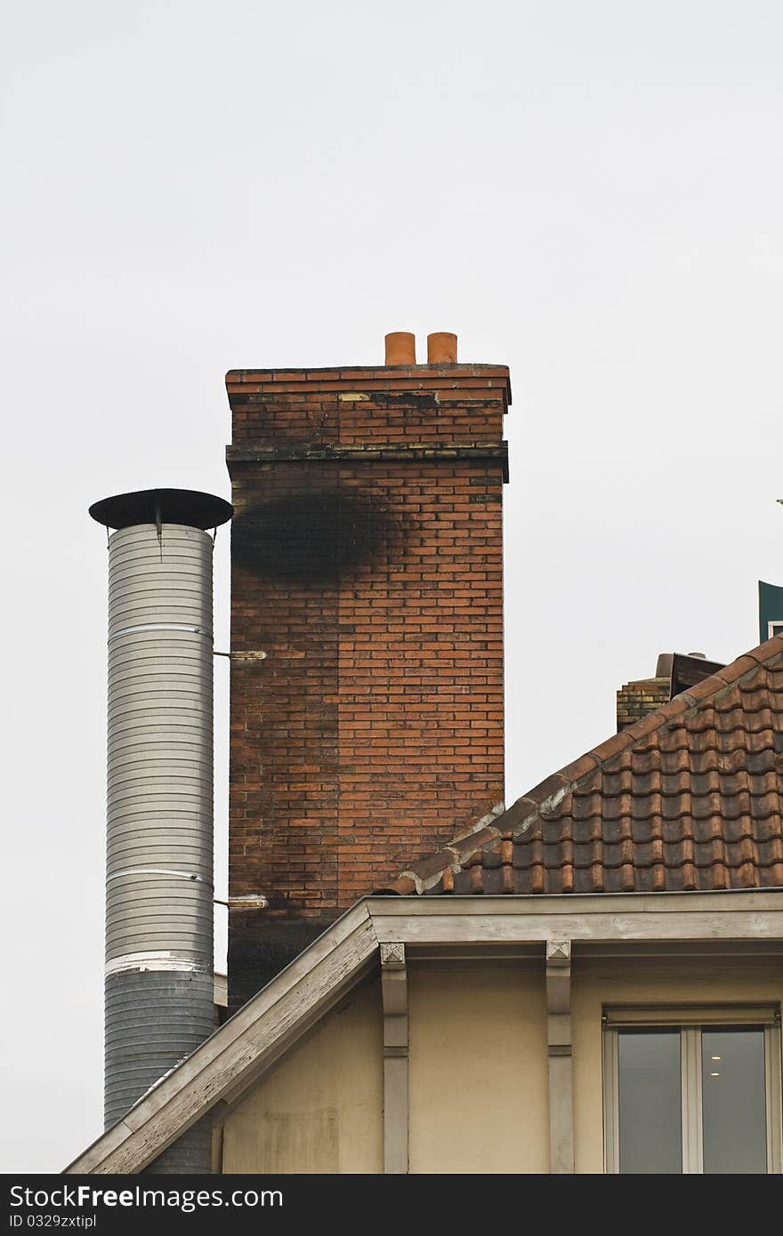 Brick chimney and metal chimney on tiled roof