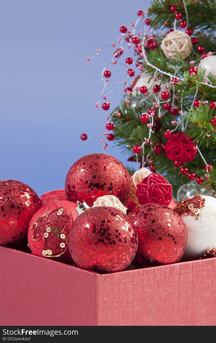 Ornaments box filled with red balls; christmass tree in the background. Ornaments box filled with red balls; christmass tree in the background