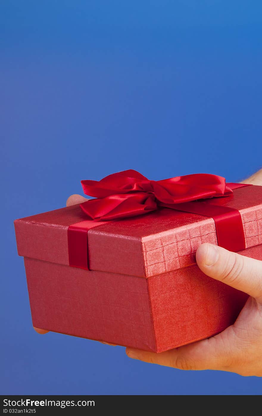 Red gift box holded with hand. shooted in studio on a blue background