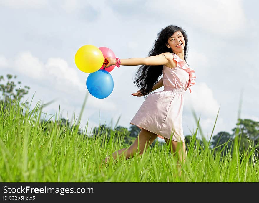 Teenage girl laughing and running holding a bunch of colorful balloons in green meadow. Teenage girl laughing and running holding a bunch of colorful balloons in green meadow