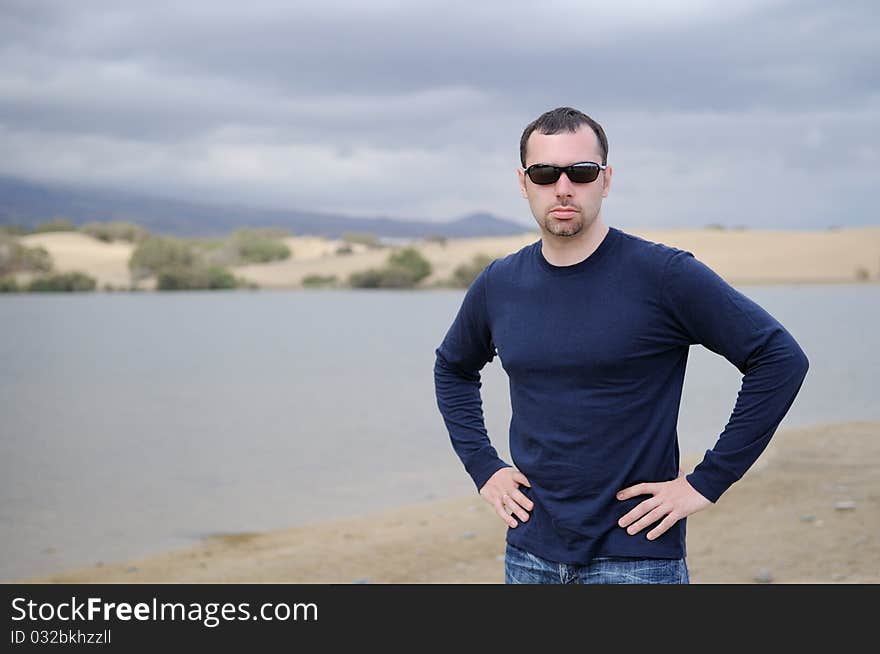 Young nice man in dark glasses on lake background before strom on Canary Island. Young nice man in dark glasses on lake background before strom on Canary Island