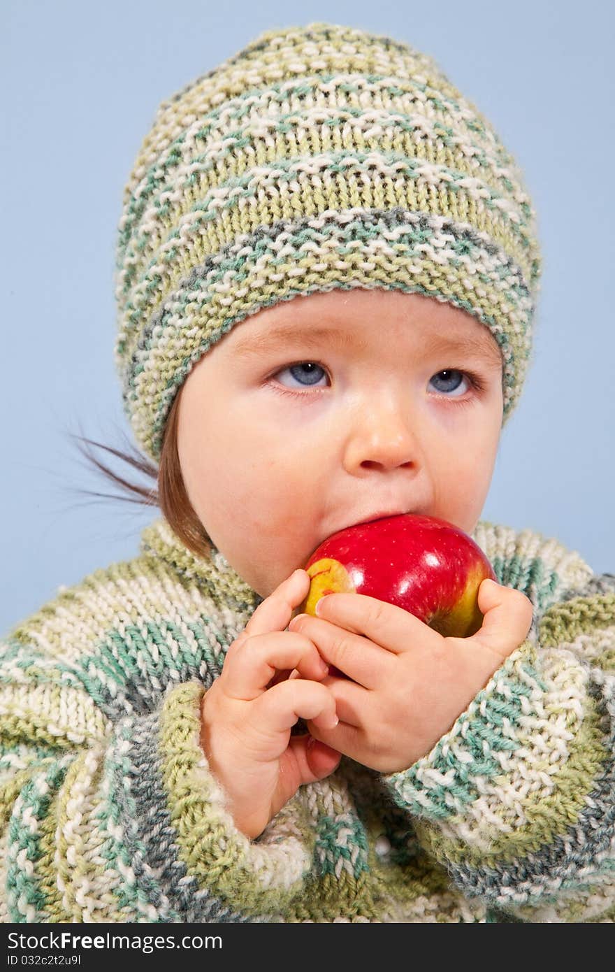 A young Boy is eating an Apple in Winter. Isolated in Studio on Blue Background.