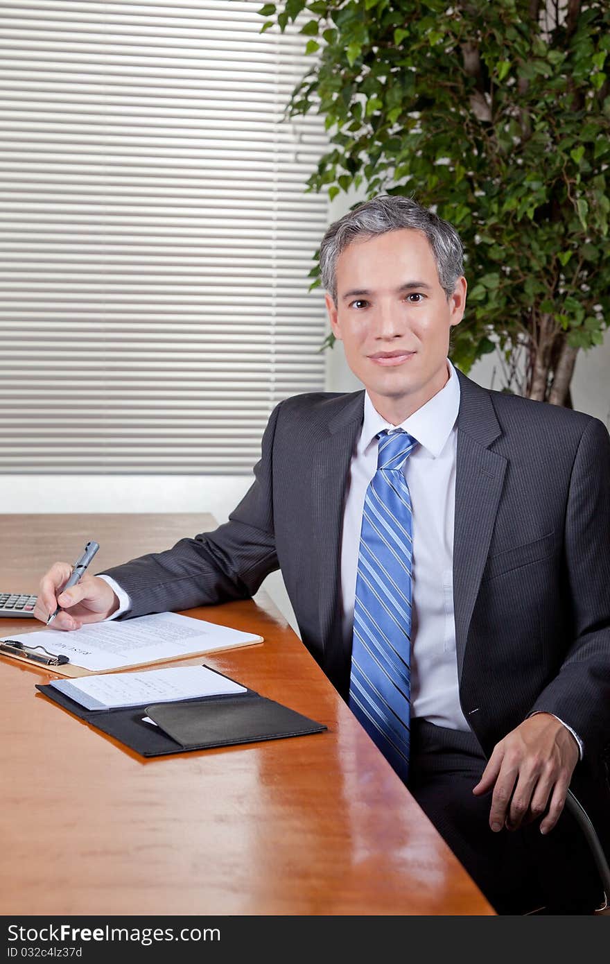 A business man in a suit takes notes while at a desk or meeting table. A business man in a suit takes notes while at a desk or meeting table