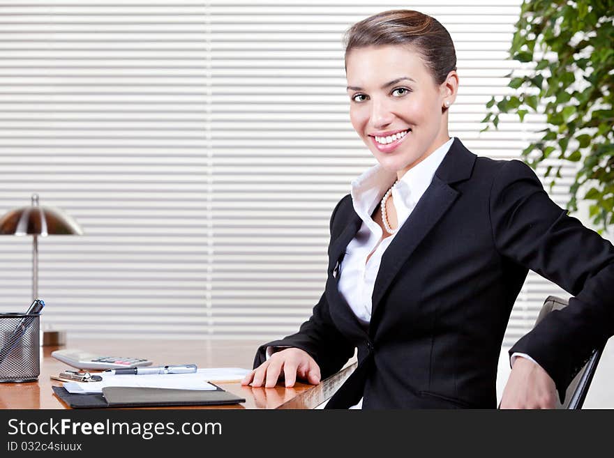 An attractive young woman happily works at her desk in her office. An attractive young woman happily works at her desk in her office