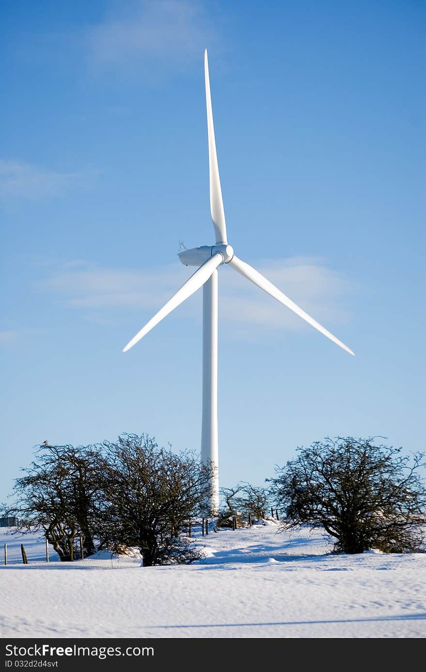 A vertical image of a snow covered field and a wind turbine