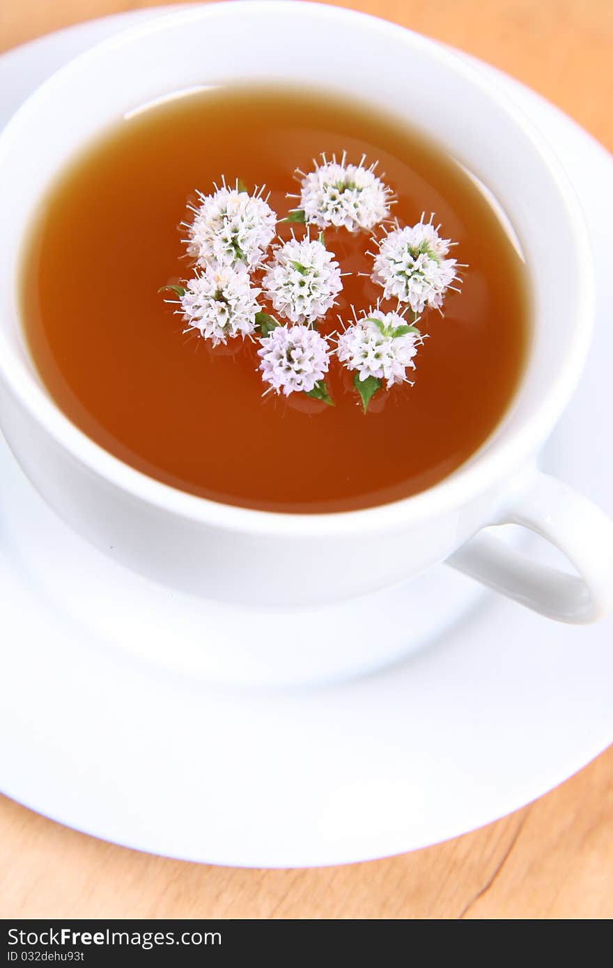 Cup of green tea with flowers of peppermint floating in it on a wooden background