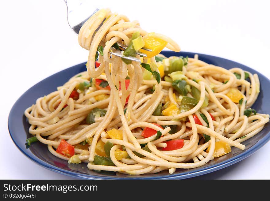 Spaghetti with vegetables being eaten with a fork on white background