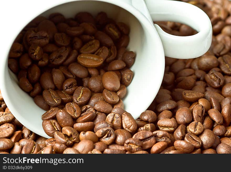 A white cup surrounded and partly filled with coffee beans. A white cup surrounded and partly filled with coffee beans