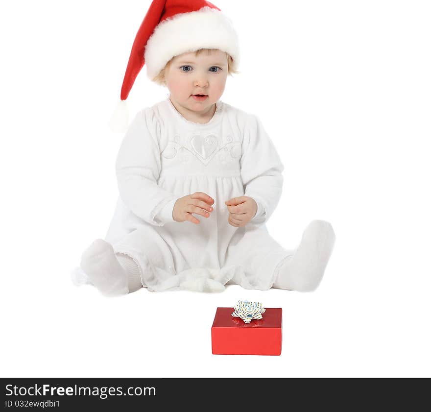 Playful baby girl in Santa's hat looking at gift in wonder. Playful baby girl in Santa's hat looking at gift in wonder