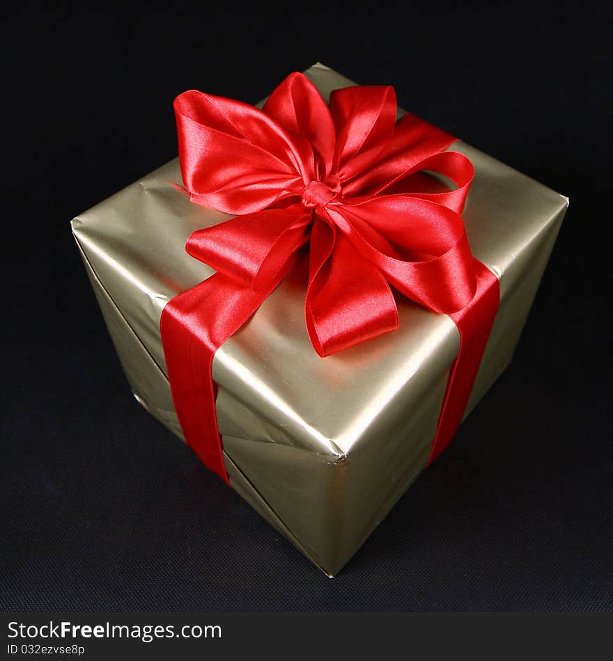 Gift in golden wrapping with red bow on black background