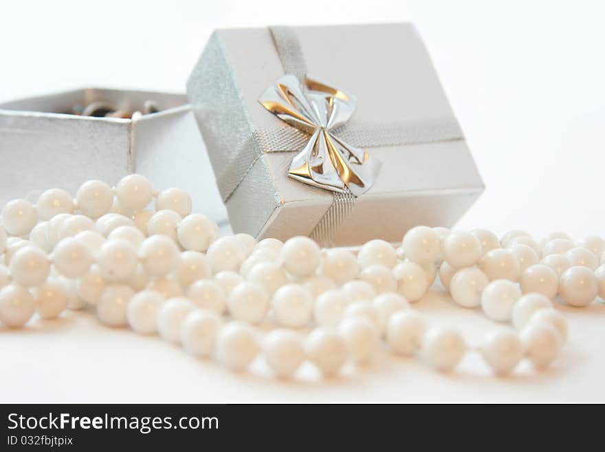 Silver gift box with a bow and white beads in the foreground. Silver gift box with a bow and white beads in the foreground