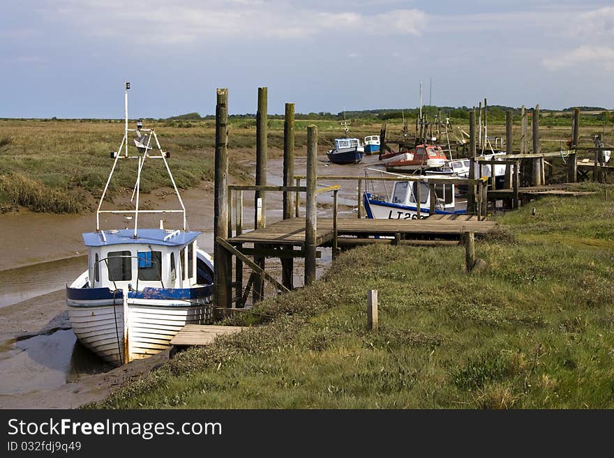 Fishing boats moored at a jetty at low tide in a channel running through the marshes of the english coast in norfolk. Fishing boats moored at a jetty at low tide in a channel running through the marshes of the english coast in norfolk