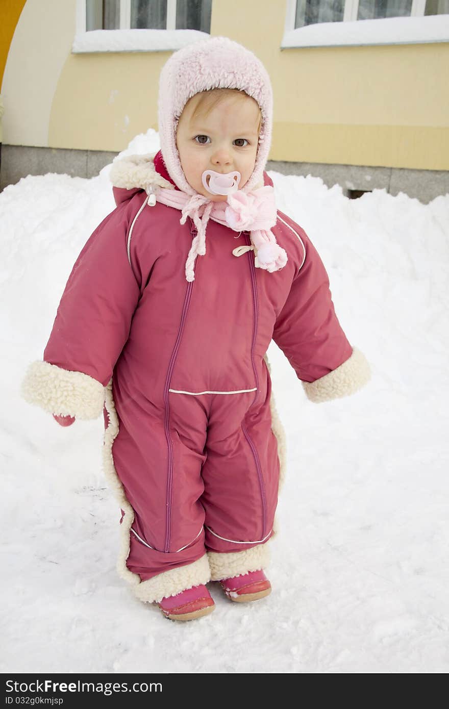 The small warmly dressed child costs in the middle of snowdrifts near a building. The small warmly dressed child costs in the middle of snowdrifts near a building