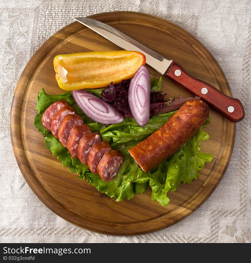 Breakfast close-up. Slices of sausage on the wooden plate with knife