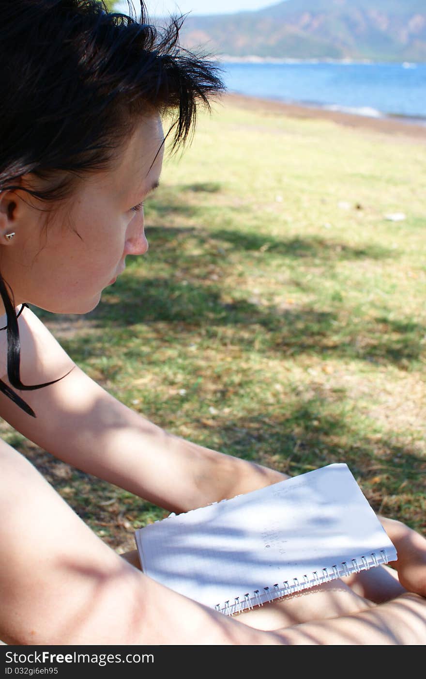 Young woman with notepad sitting on the beach