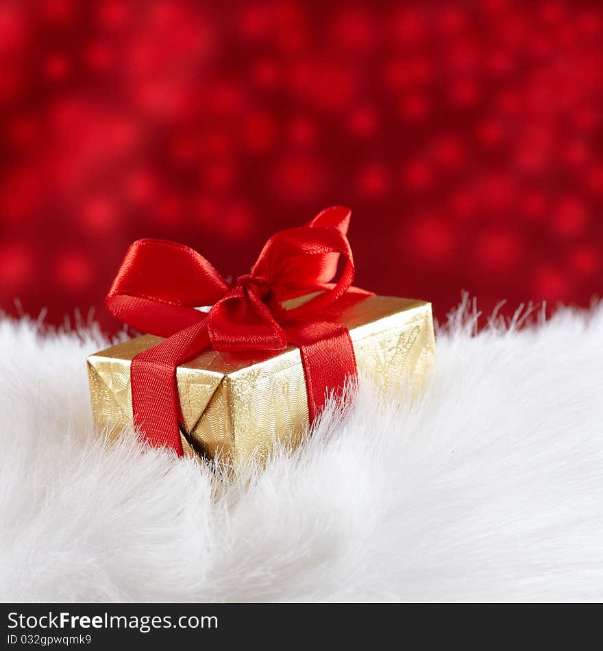 Golden gift box on white fur against red blurred