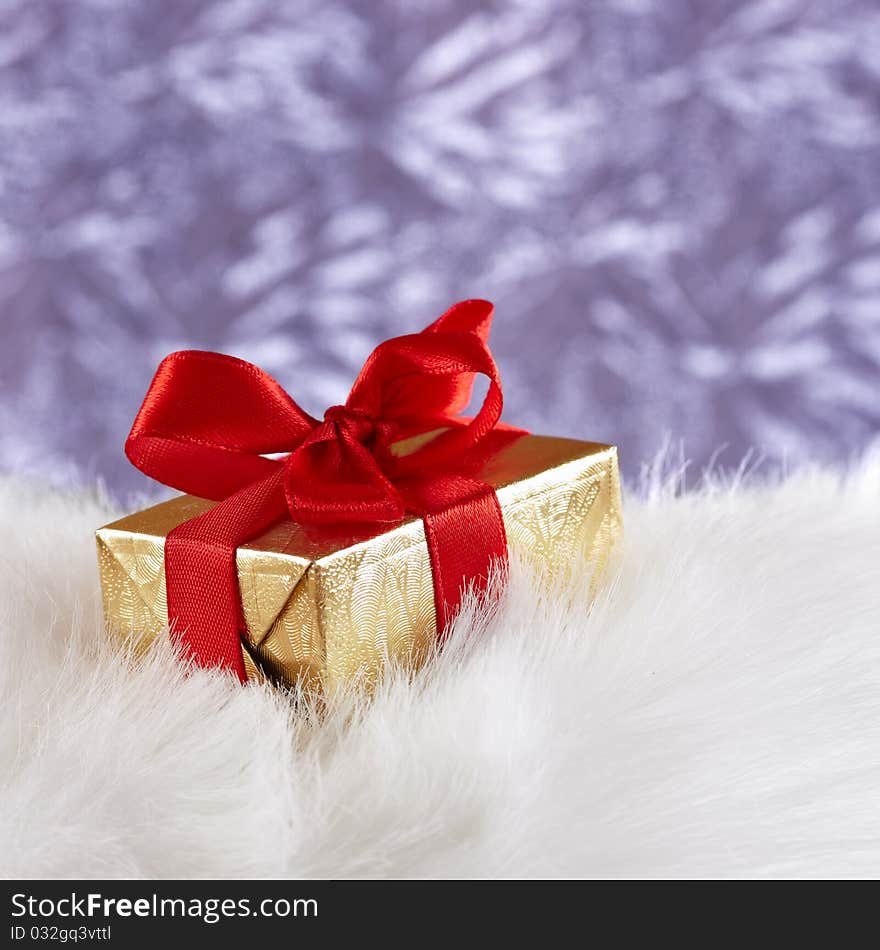 Golden gift box on white fur against blue blurre