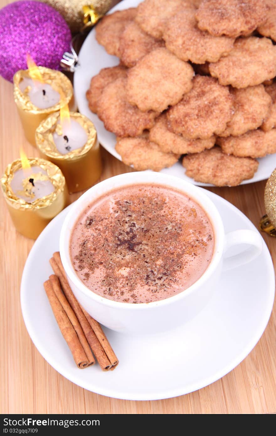 Cup of hot chocolate with cinnamon, cinnamon cookies and gold candles with christmas balls in the background. Cup of hot chocolate with cinnamon, cinnamon cookies and gold candles with christmas balls in the background