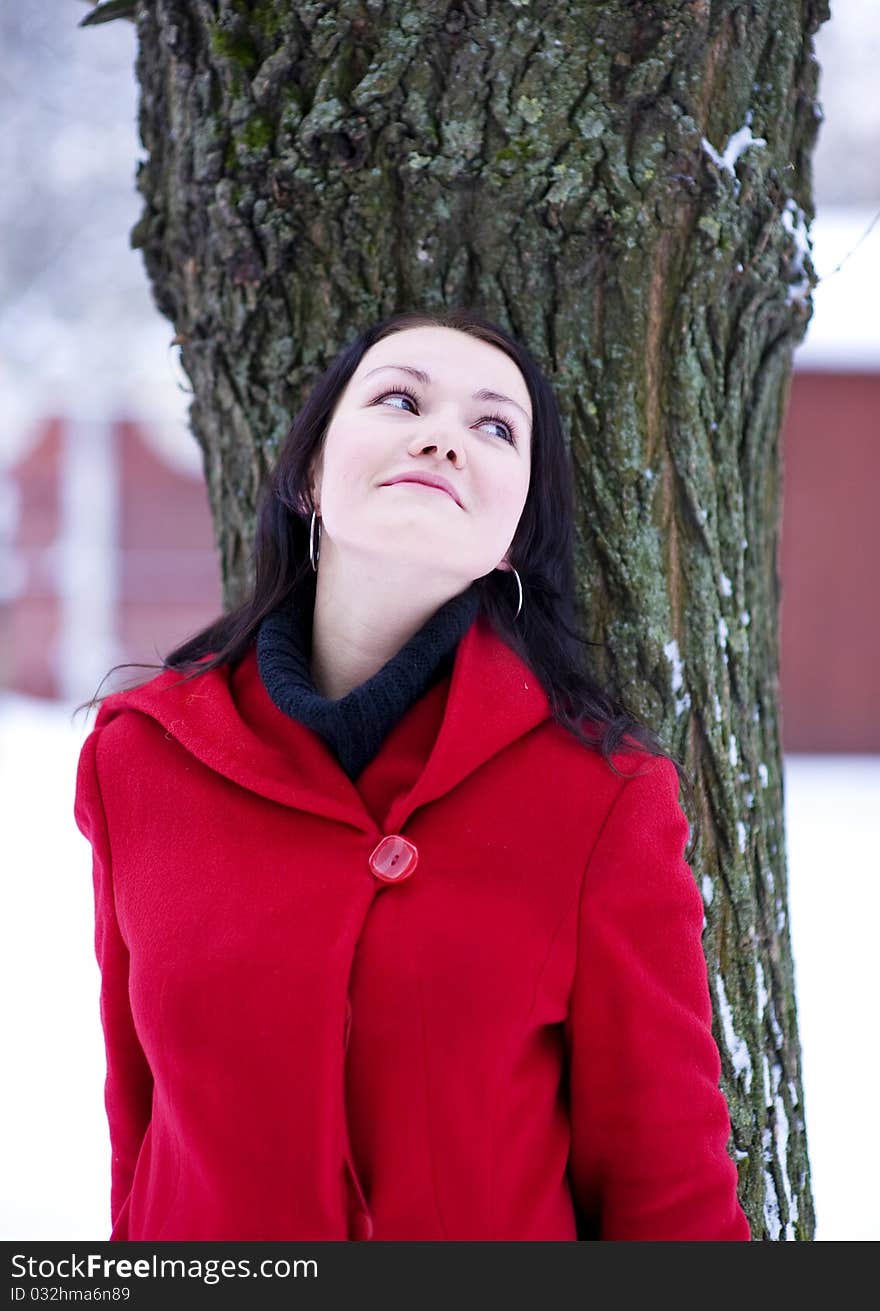 Young beautiful girl in the red coat leaning the tree. Young beautiful girl in the red coat leaning the tree