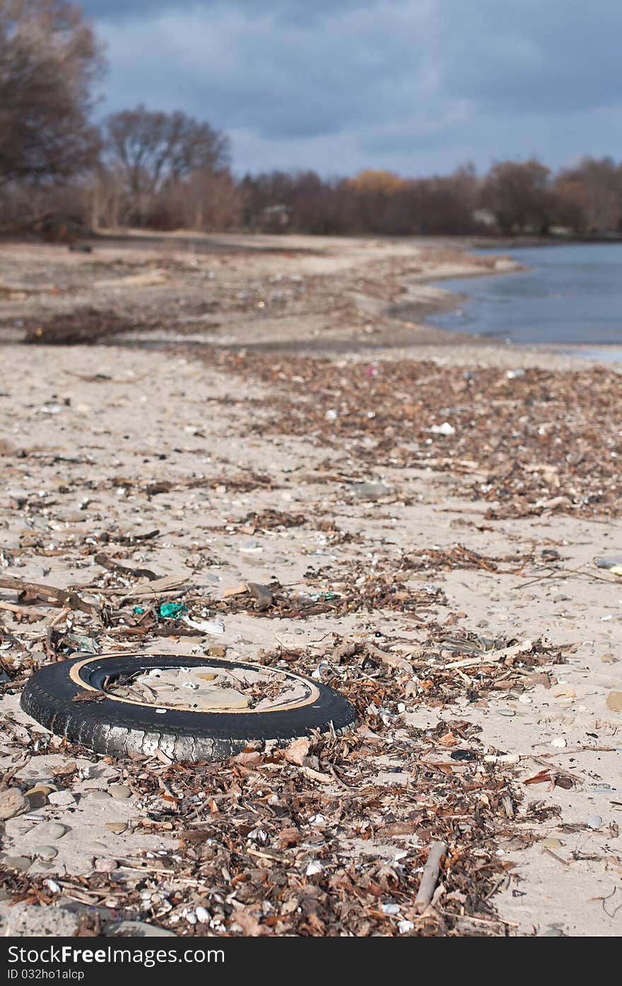 An old tire lies buried in the sand on a beach surrounded by other garbage. An old tire lies buried in the sand on a beach surrounded by other garbage.