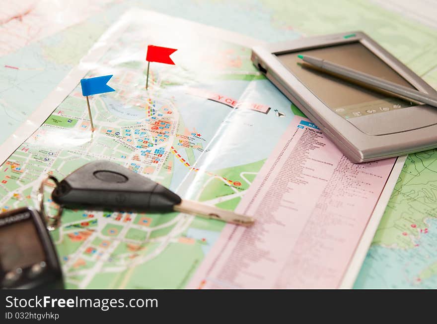 Road map with a red and blue flag, car keys, electronic organizer and credit cards. closeup. Road map with a red and blue flag, car keys, electronic organizer and credit cards. closeup.