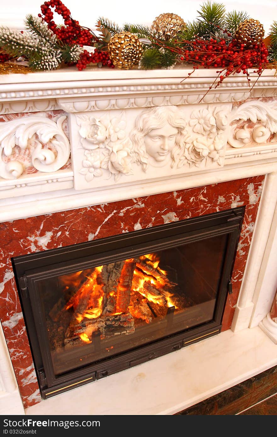 Christmas ornaments on a marble fireplace. In a fireplace fire burns.