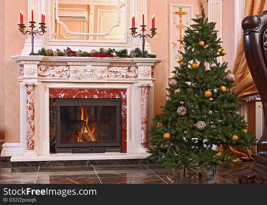 Candles in a candlestick on a fireplace in a spacious hall with a Christmas fur-tree.