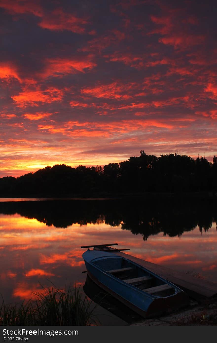 Red sunrise over a river. The boat at the pier before going out on fishing. Red sunrise over a river. The boat at the pier before going out on fishing