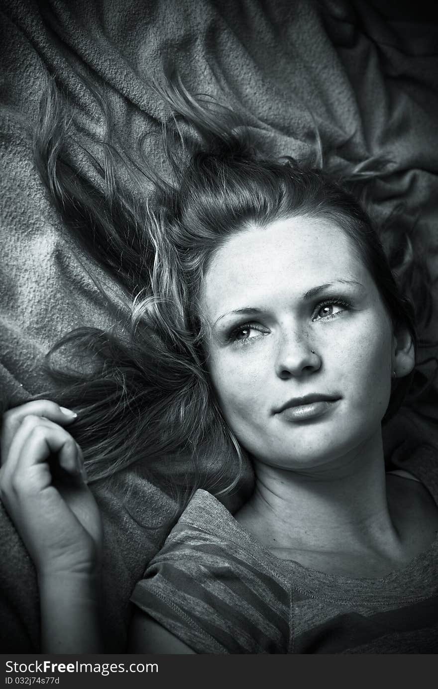 Portrait of a girl with a retro style monochrome retouching laying on a bed,holding her hair and looking very thoughtfull. Portrait of a girl with a retro style monochrome retouching laying on a bed,holding her hair and looking very thoughtfull