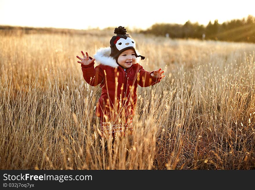 A cute girl toddler running through a field at sunset laughing and having a great time in her red winter coat and adorable penguin hat. A cute girl toddler running through a field at sunset laughing and having a great time in her red winter coat and adorable penguin hat.