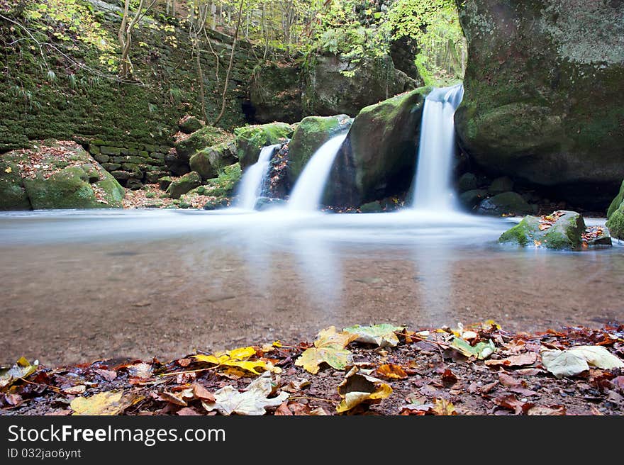 Autumn forest waterfall falling from the mossy rocks