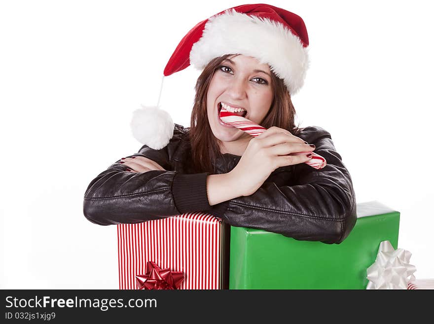 A woman with a Santa hat is leaning on some presents eating a peppermint stick. A woman with a Santa hat is leaning on some presents eating a peppermint stick.