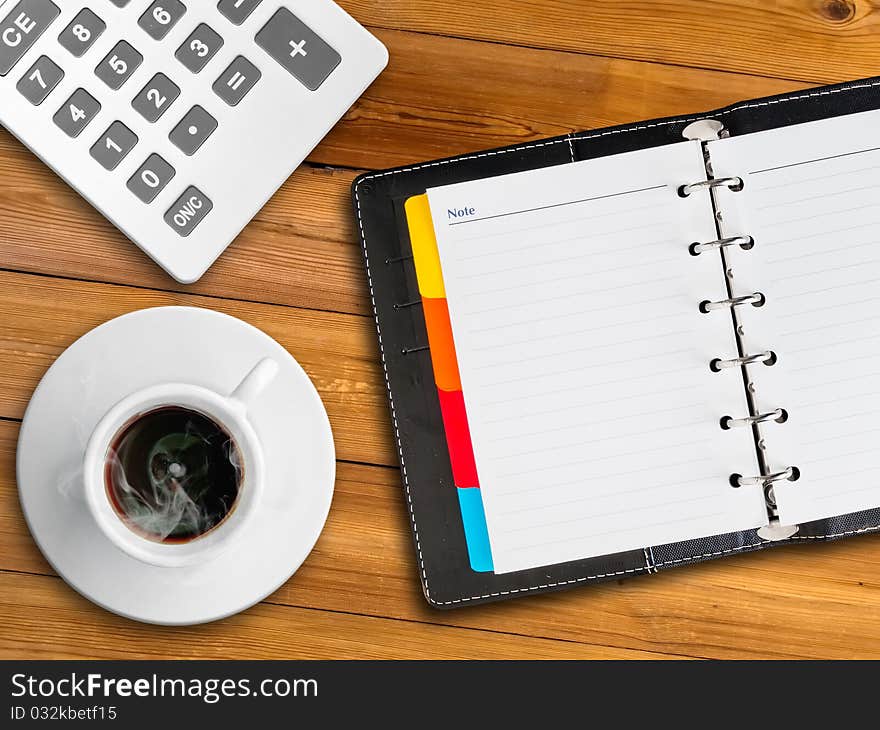 White calculator and white notebook and white cup of hot coffee on wood table