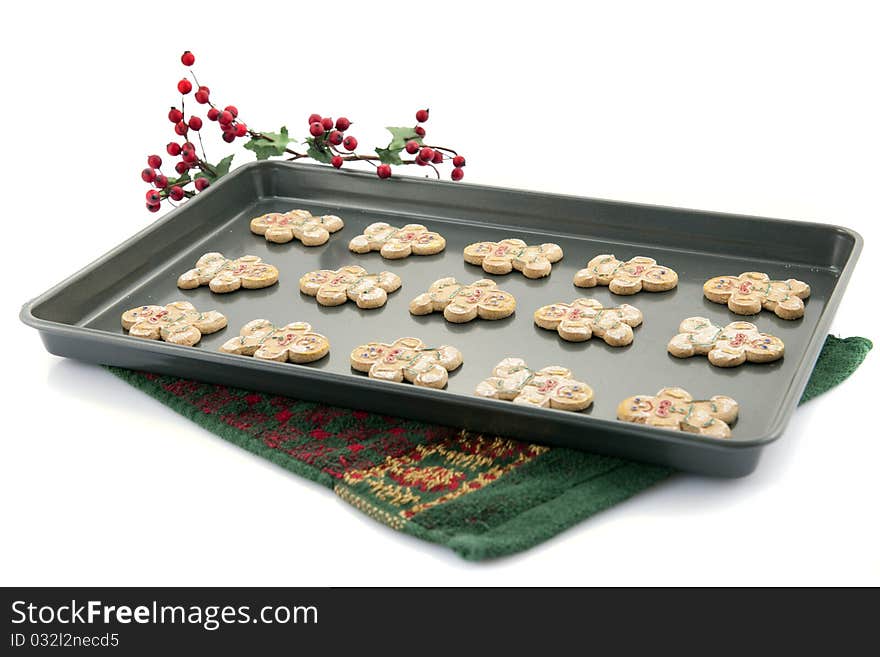 A cookie sheet containing 15 gingerbread cookies on a Christmas-colored terry towel.  Isolated on white.