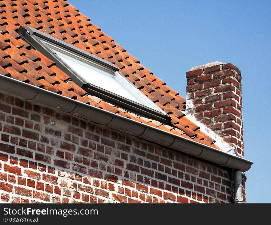 Roof and wall of a brick building with a window on a blue sky