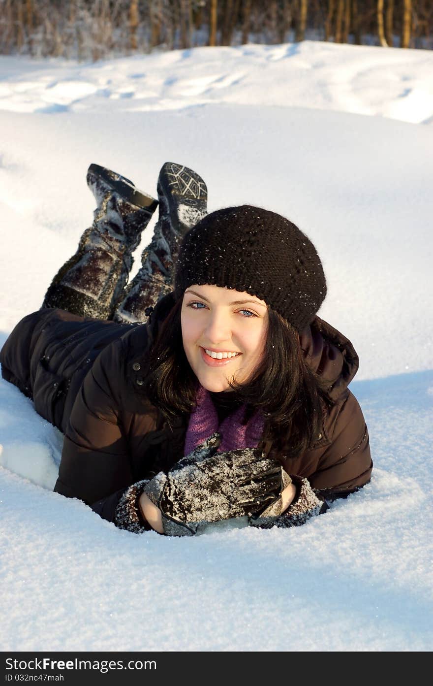 Happy young woman laying in the snow in winter forest