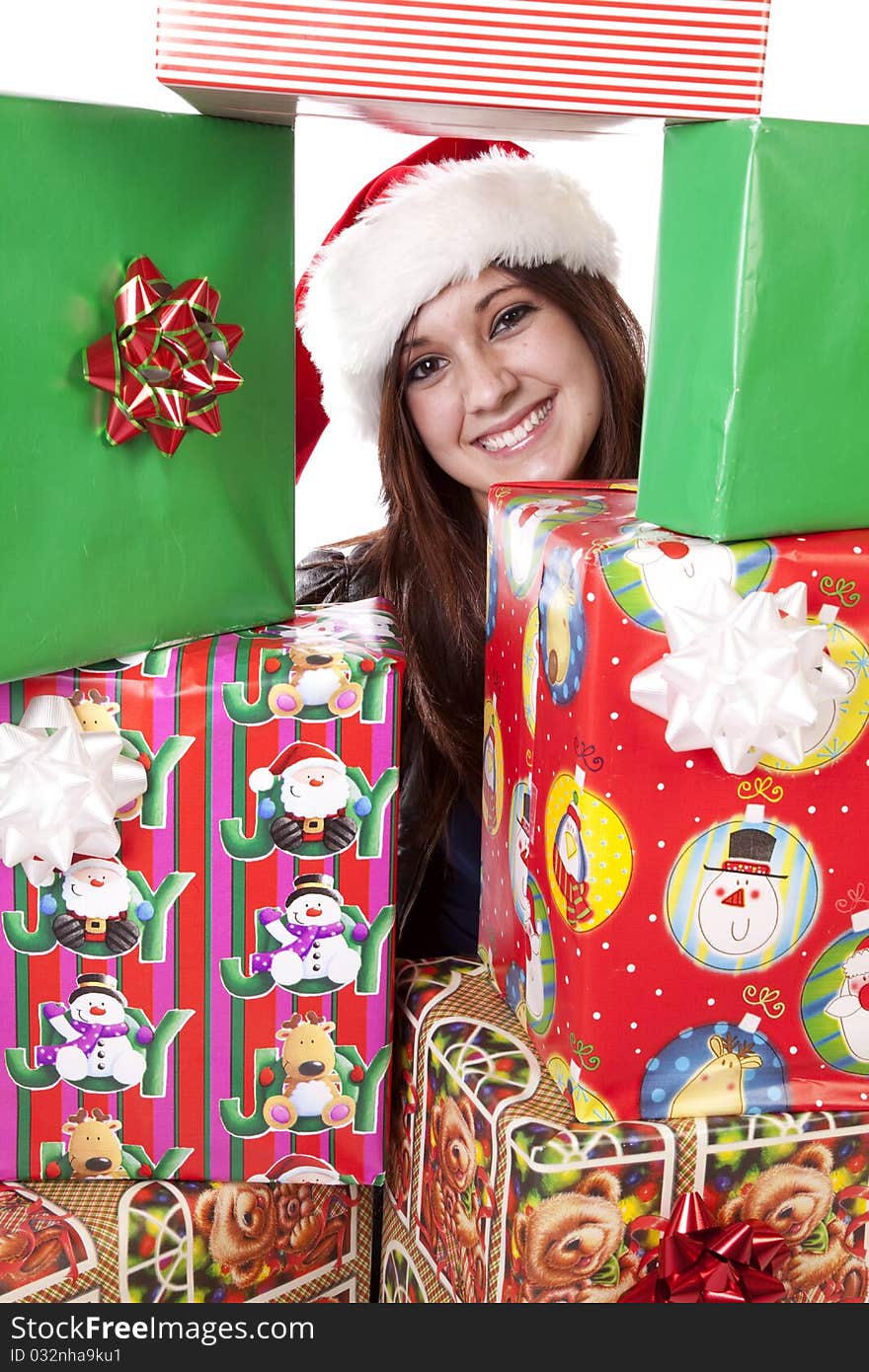 A woman with her face looking through a stack of presents while wearing her Santa hat. A woman with her face looking through a stack of presents while wearing her Santa hat.