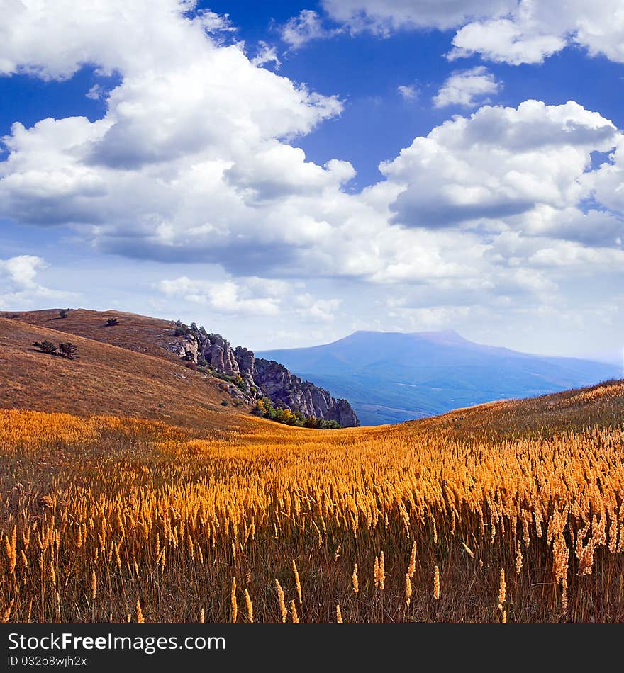 Mountain landscape with meadow and white clouds on blue sky background. Mountain landscape with meadow and white clouds on blue sky background.