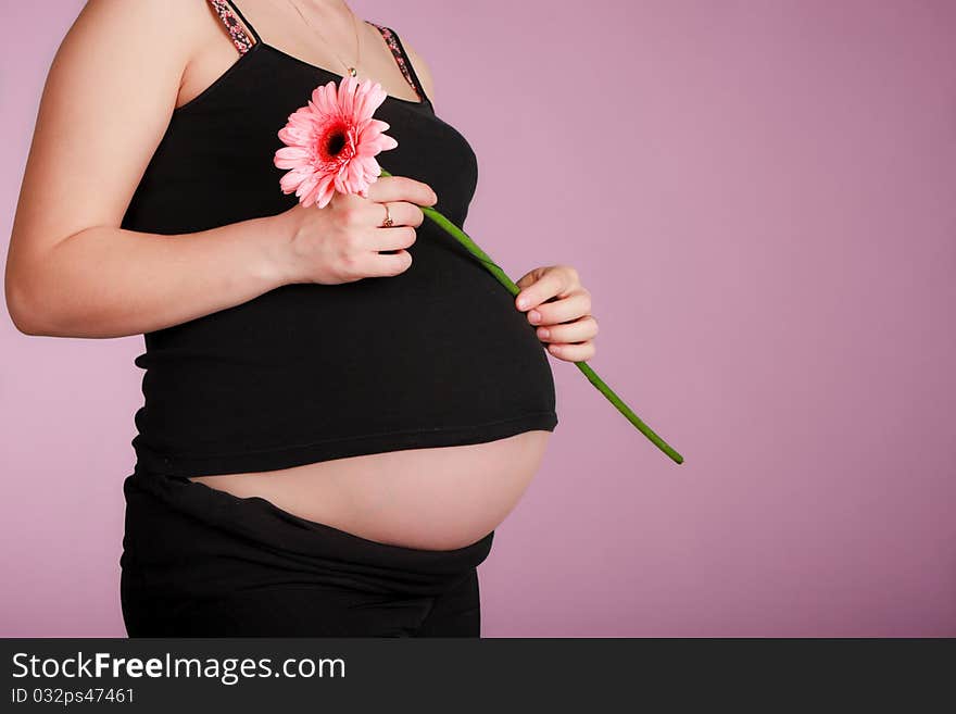 Beautiful pregnant woman with flower on pink background