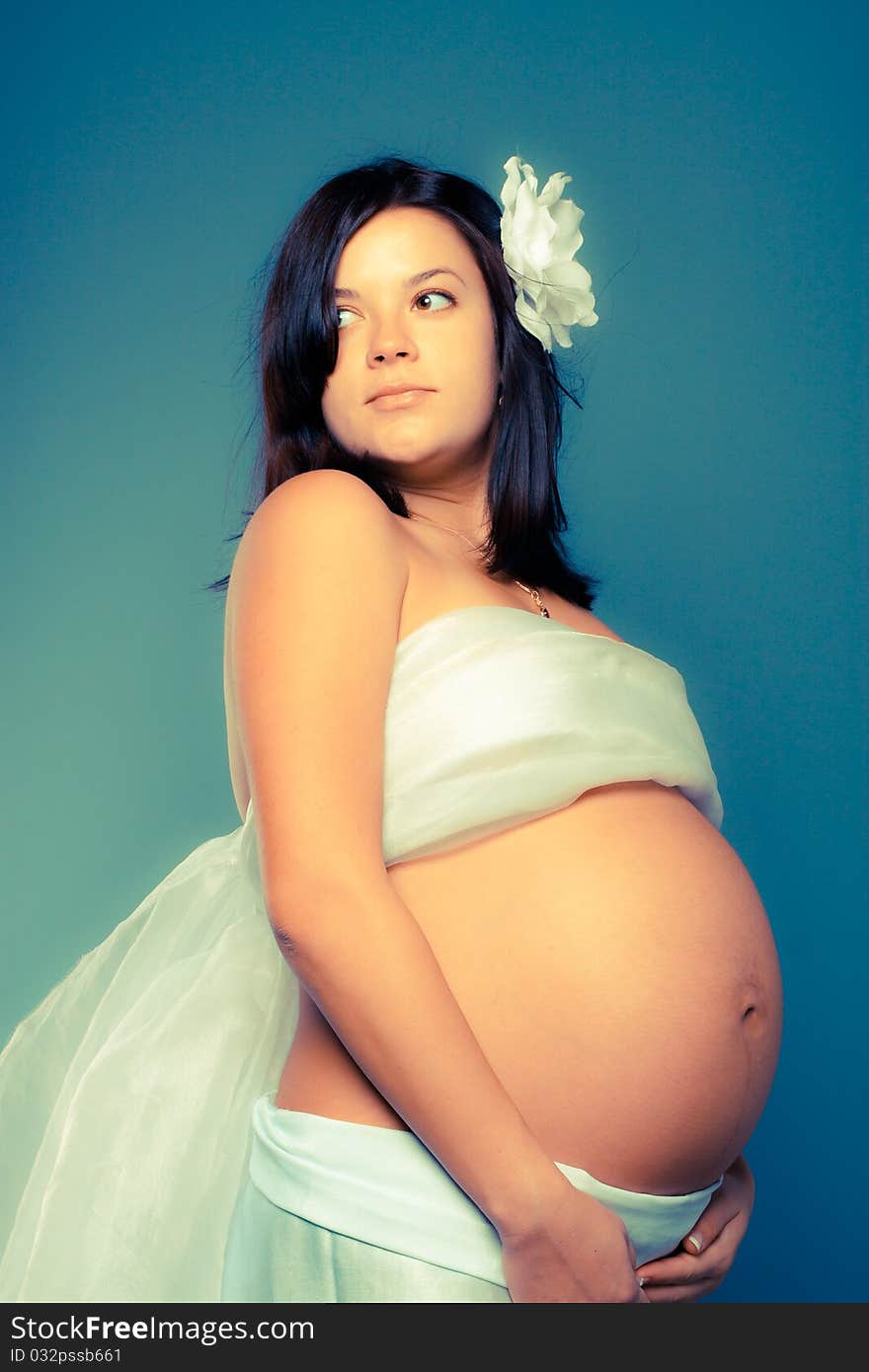 Beautiful pregnant woman staing on grey background. Toned as cross-procesed photos