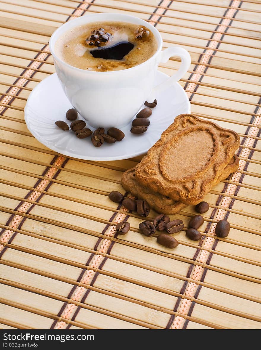 Cup of capuchino with coffee beans and cookie on a mat