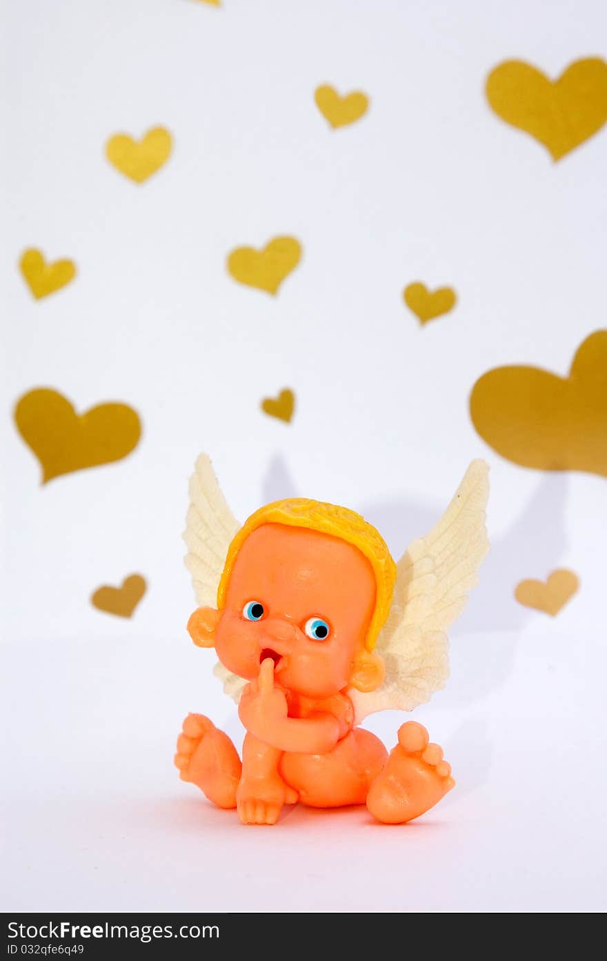 Funny shy toy angel puts his finger in mouth on white background with golden hearts. Funny shy toy angel puts his finger in mouth on white background with golden hearts