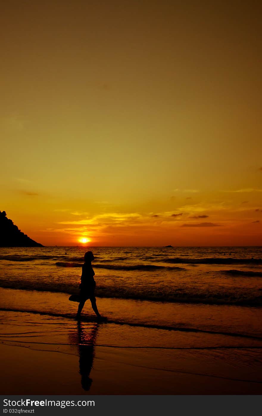 The sun sets in the sea with a silhouette of a girl walking at the coastline. The sun sets in the sea with a silhouette of a girl walking at the coastline.